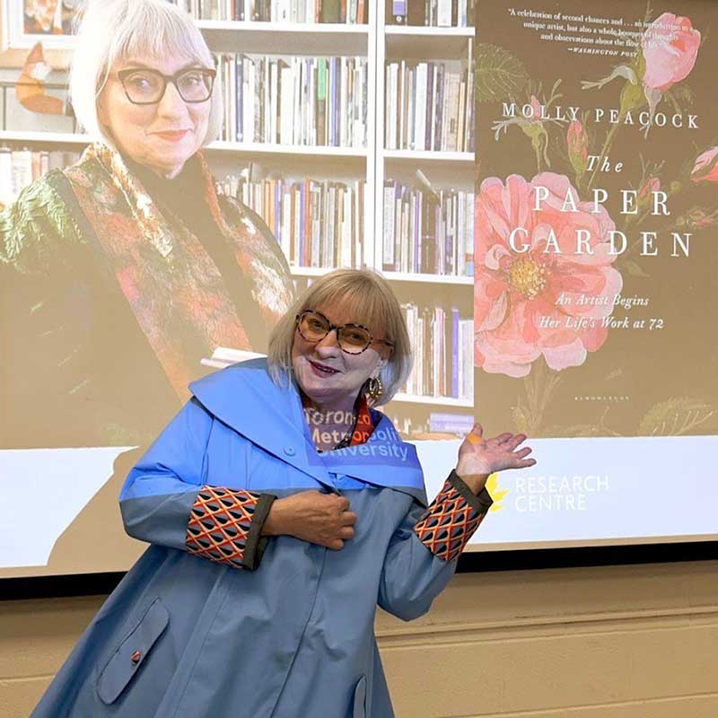 A person in a blue coat standing in front of a large projector screen